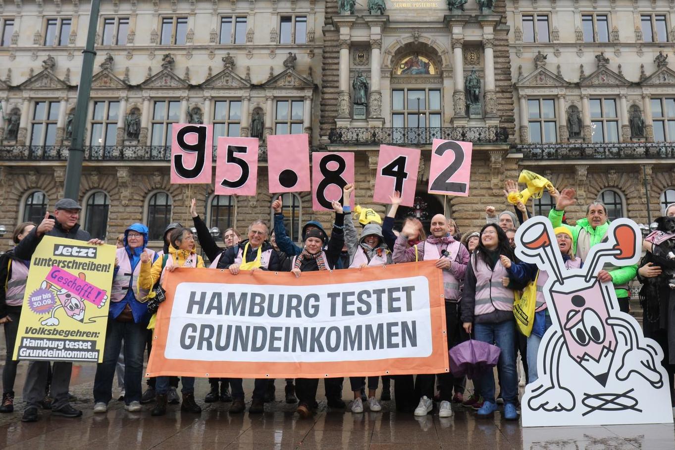 Menschen feiern vor dem Rathaus Hamburg mit Schildern, auf denen die Zahl der abgegebenen Unterschriften steht.